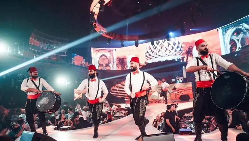 Dabke dancers in red fez and sashes with big drums performing on a stage in Dubai